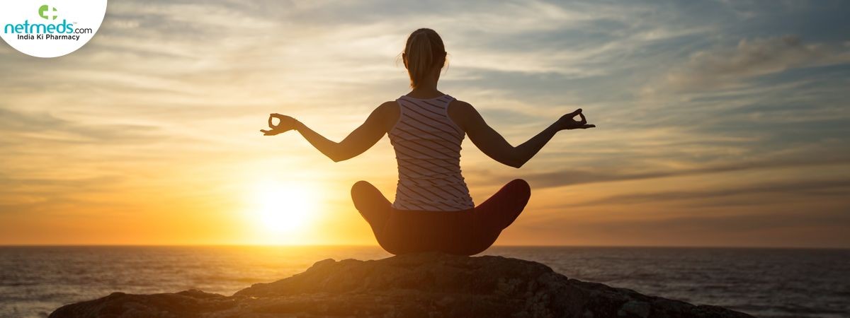 Silhouette of a person meditating on a rock by the sea during sunset.